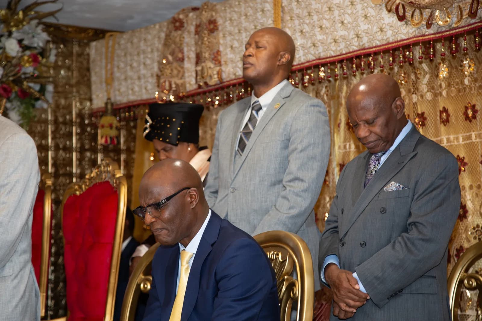 Seated and standing leaders bow solemnly in a moment of prayer