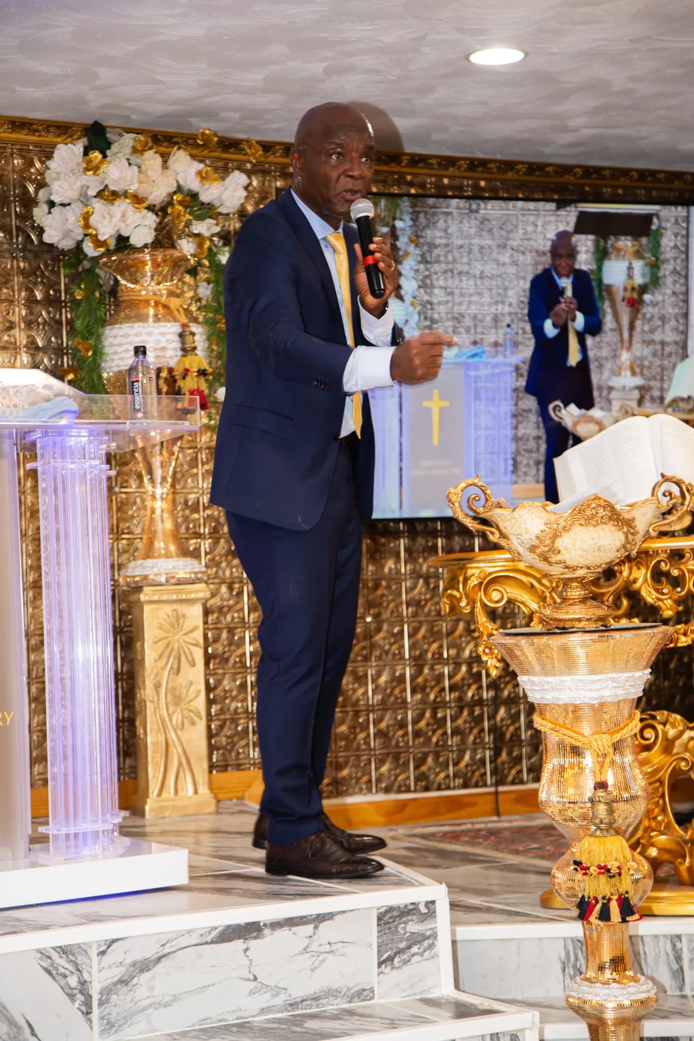 Pastor stands full-frame at the lectern with mic raised