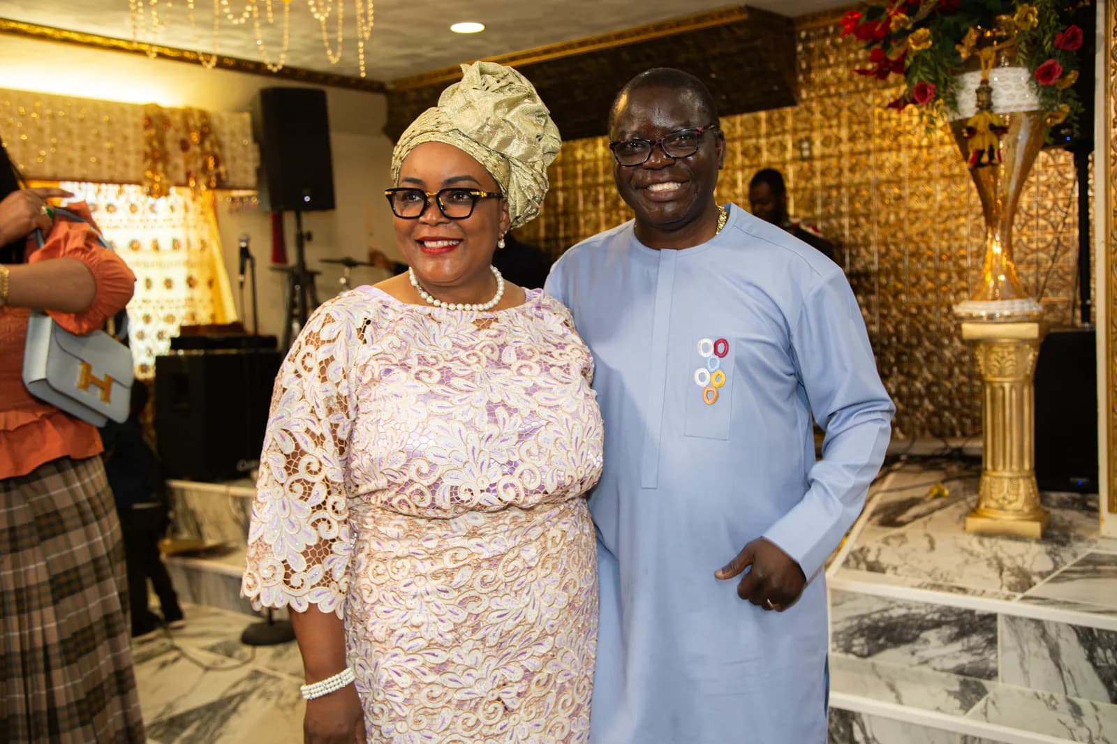 The founding couple stands together smiling — pastor in sky-blue agbada