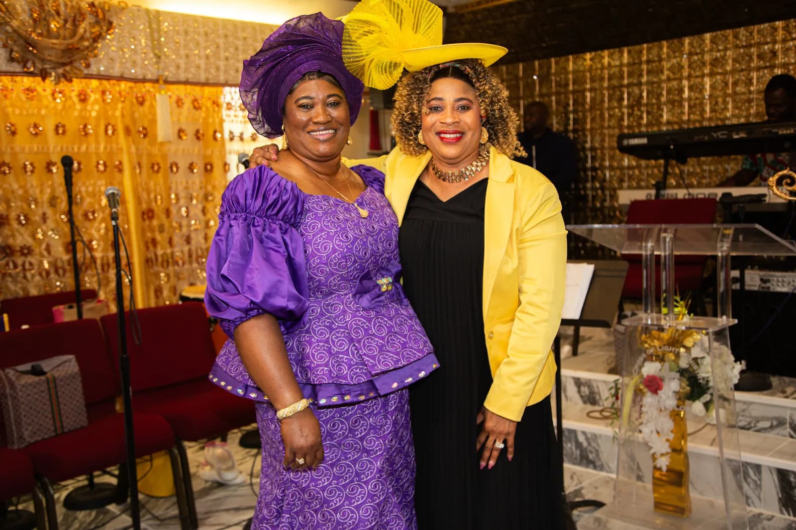 Two women in complementary purple and yellow outfits embrace